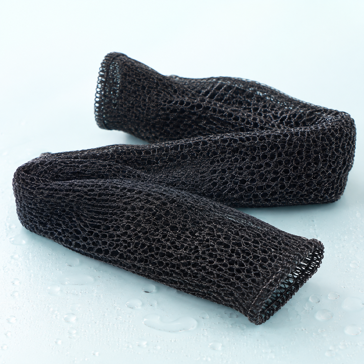 Two black Nyla mesh bath sponges on a clean aqua surface